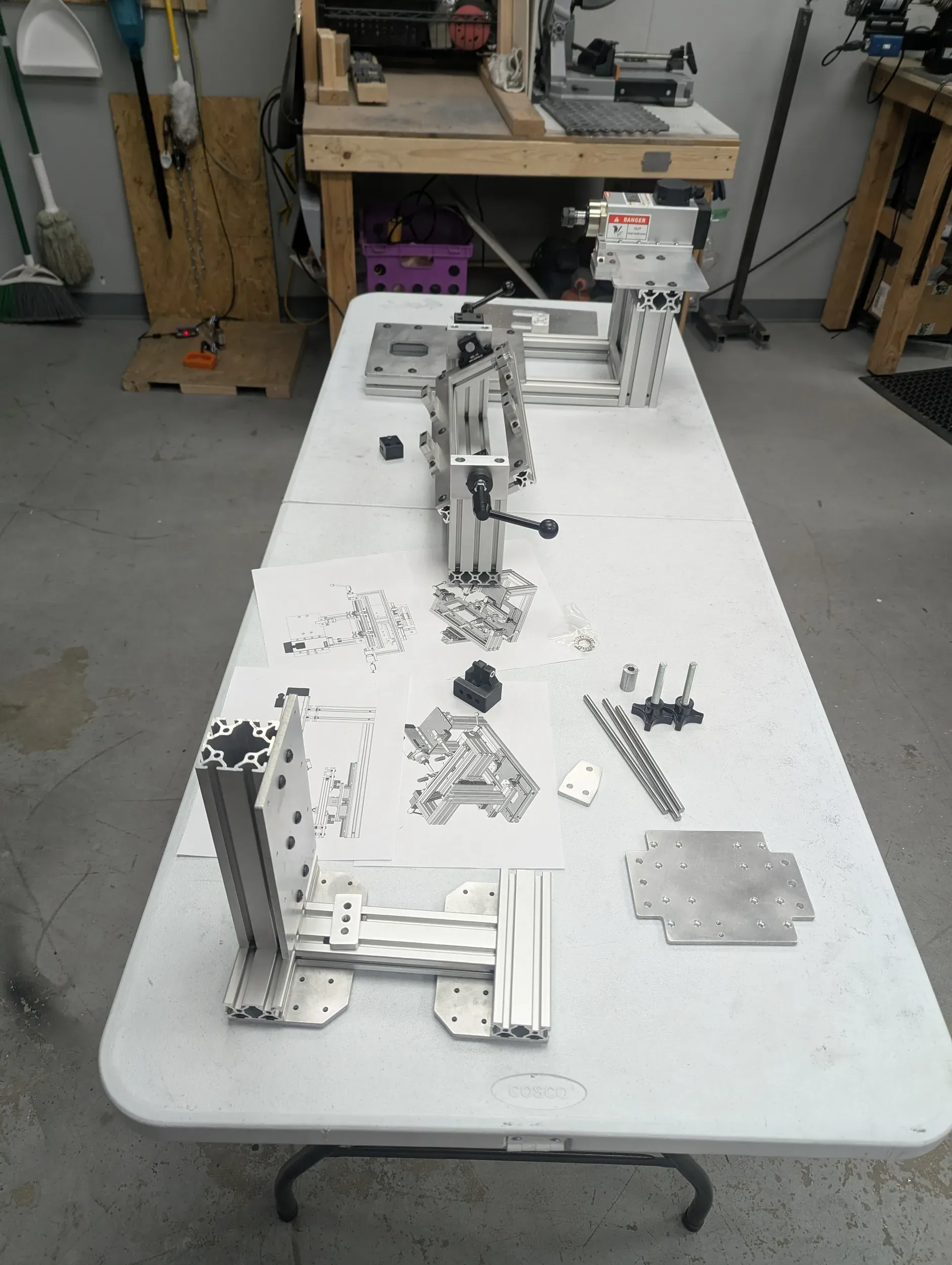 T-slot frame parts laid out on a shop table beside their assembly drawings